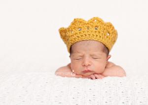 newborn boy wearing a gold crown for his portrait shoot in home