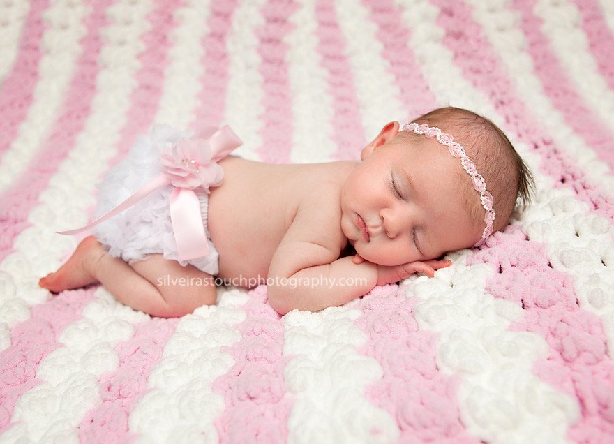 Newborn photo of baby girl sleeping on a pink striped blanket