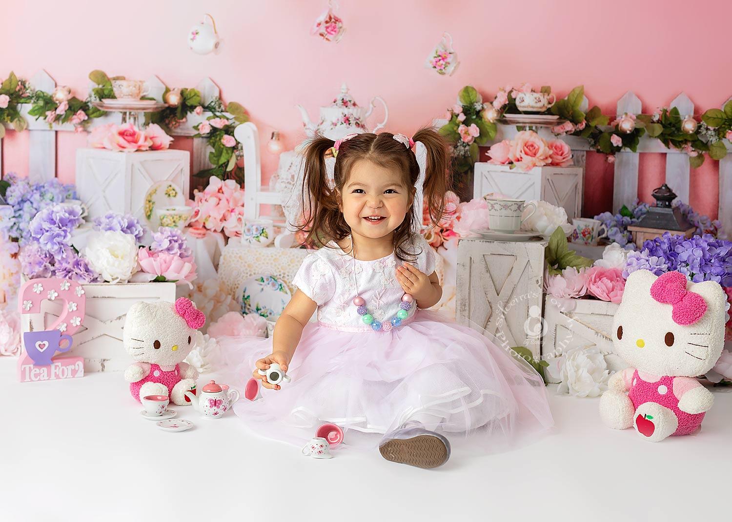 Pink and white girl tea party setup with plush Hello Kitty toys, floral decorations, and a joyful toddler in a pastel dress, capturing adorable baby and maternity photos in NJ.
