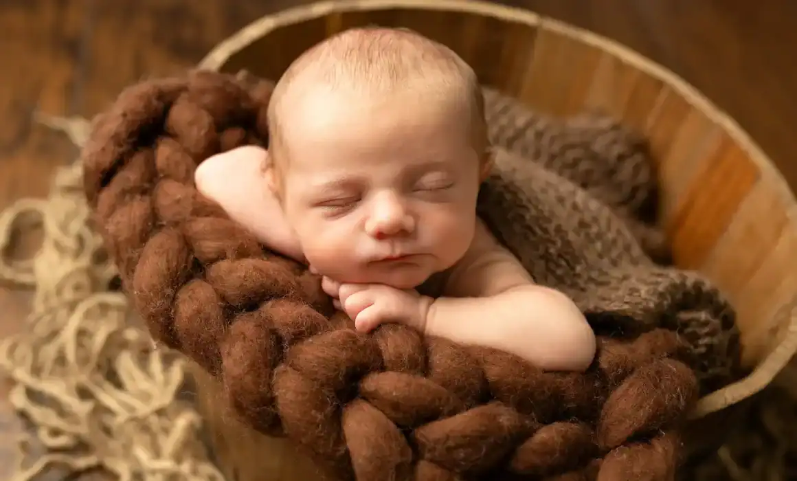 Newborn boy pictured in a wooden bucket with hands on chin