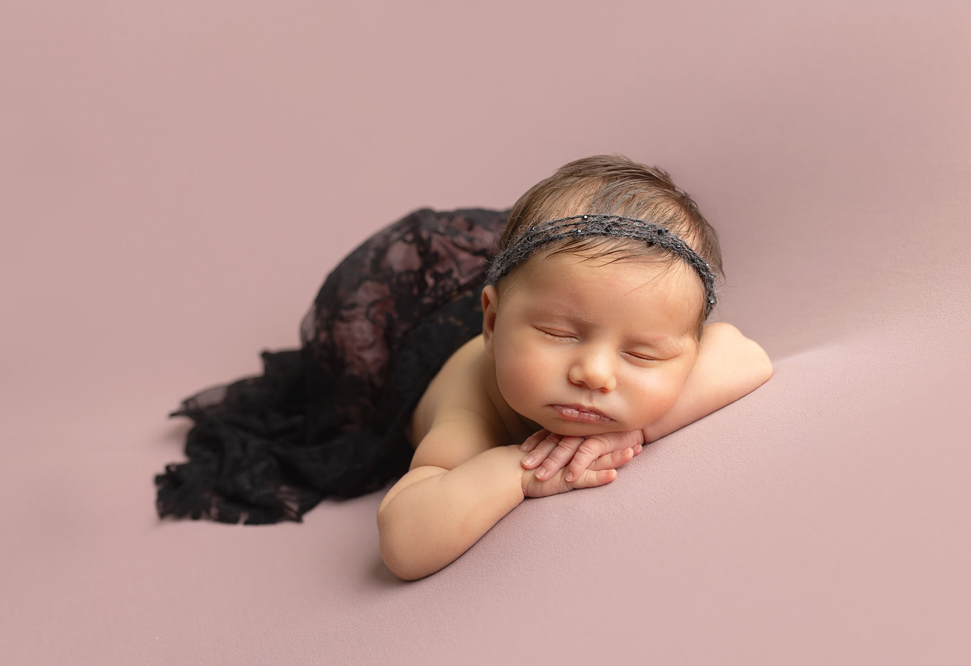newborn portrait session in studio of baby wearing lace wrap and pink backdrop