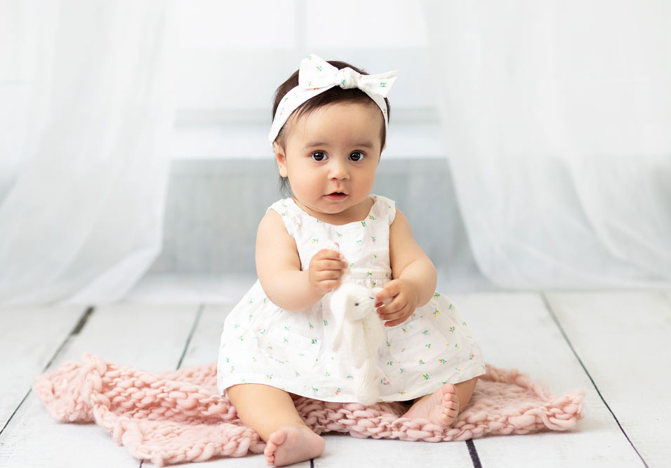 Baby sitting in portrait studio dressed in white dress