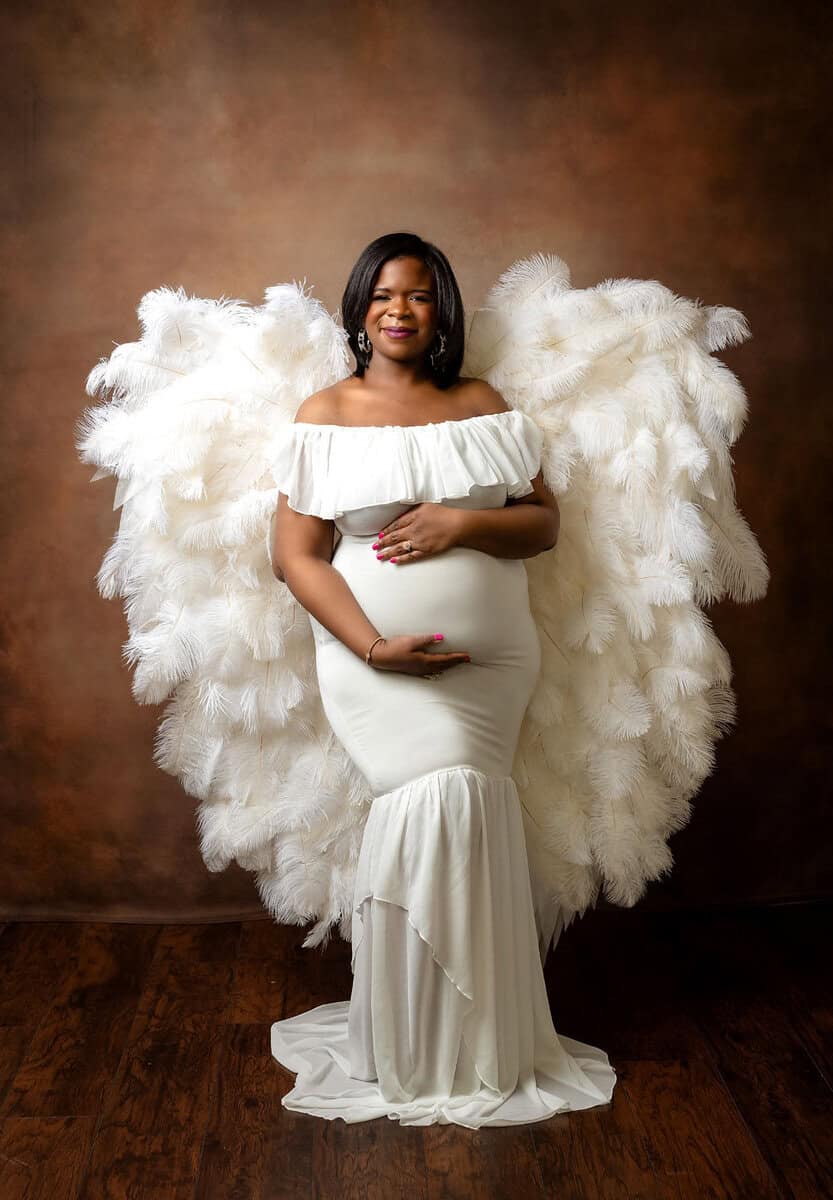 Mom to be wearing angel wings and white gown during maternity shoot