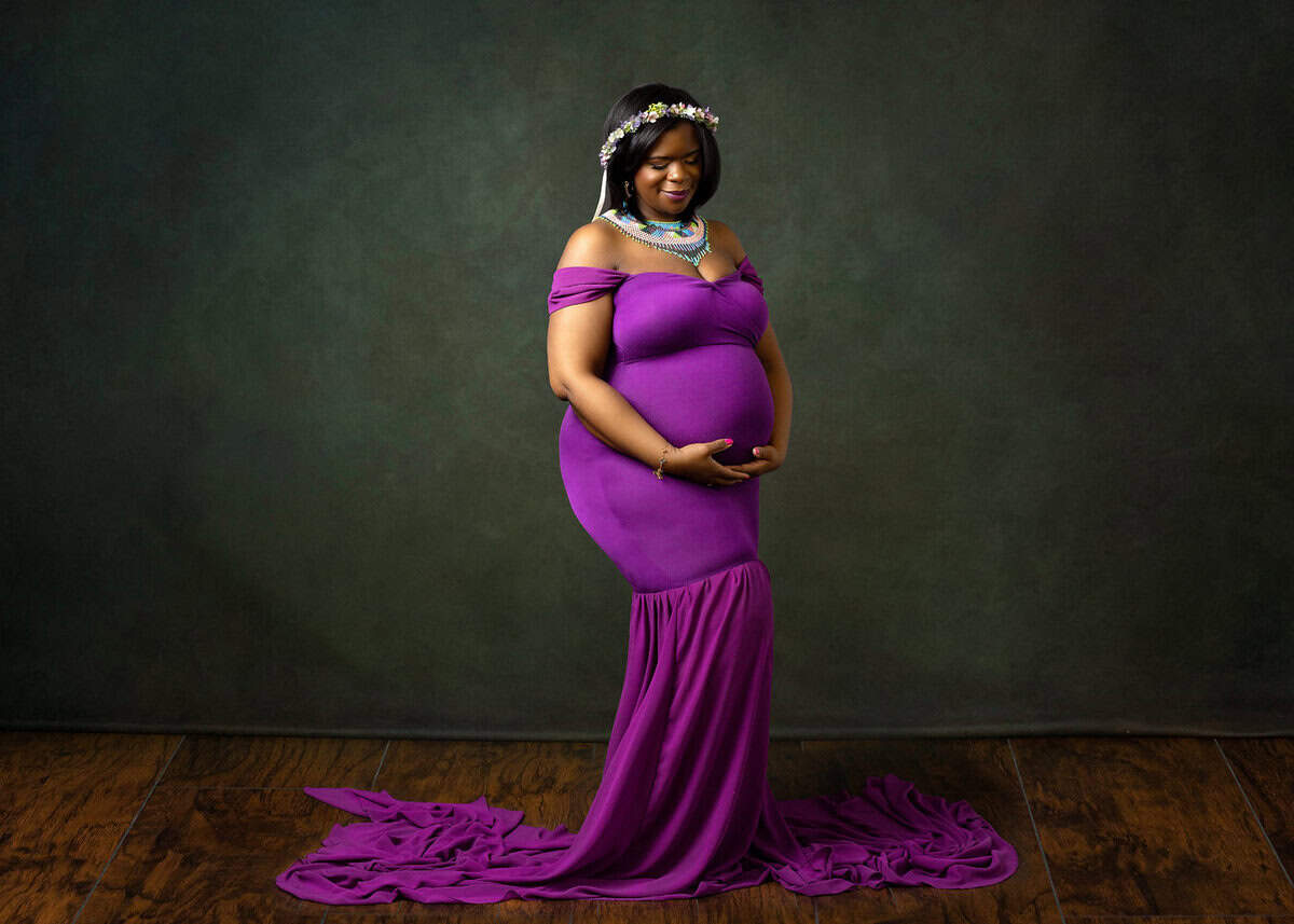 pregnancy photo shoot near me pregnant mom cradling her baby bump wearing purple gown smiling