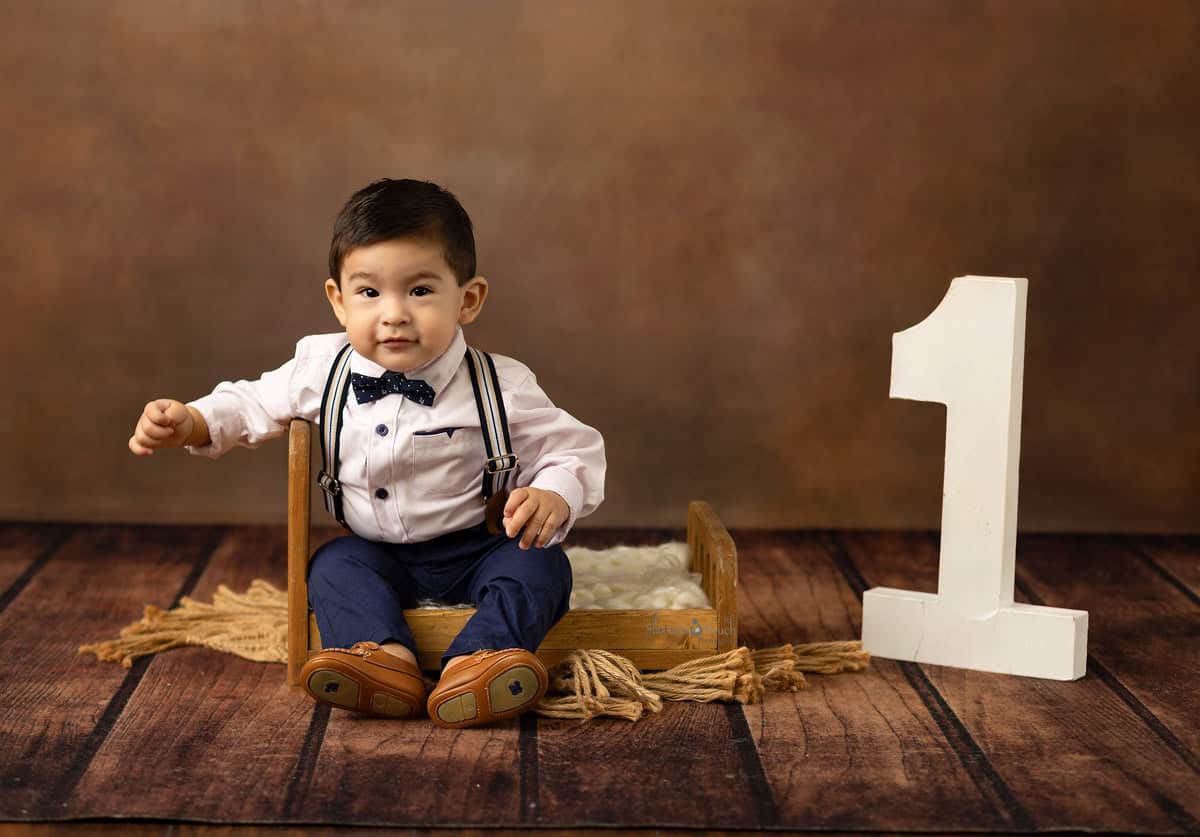 Baby boy sitting on a small prop bed for his birthday session