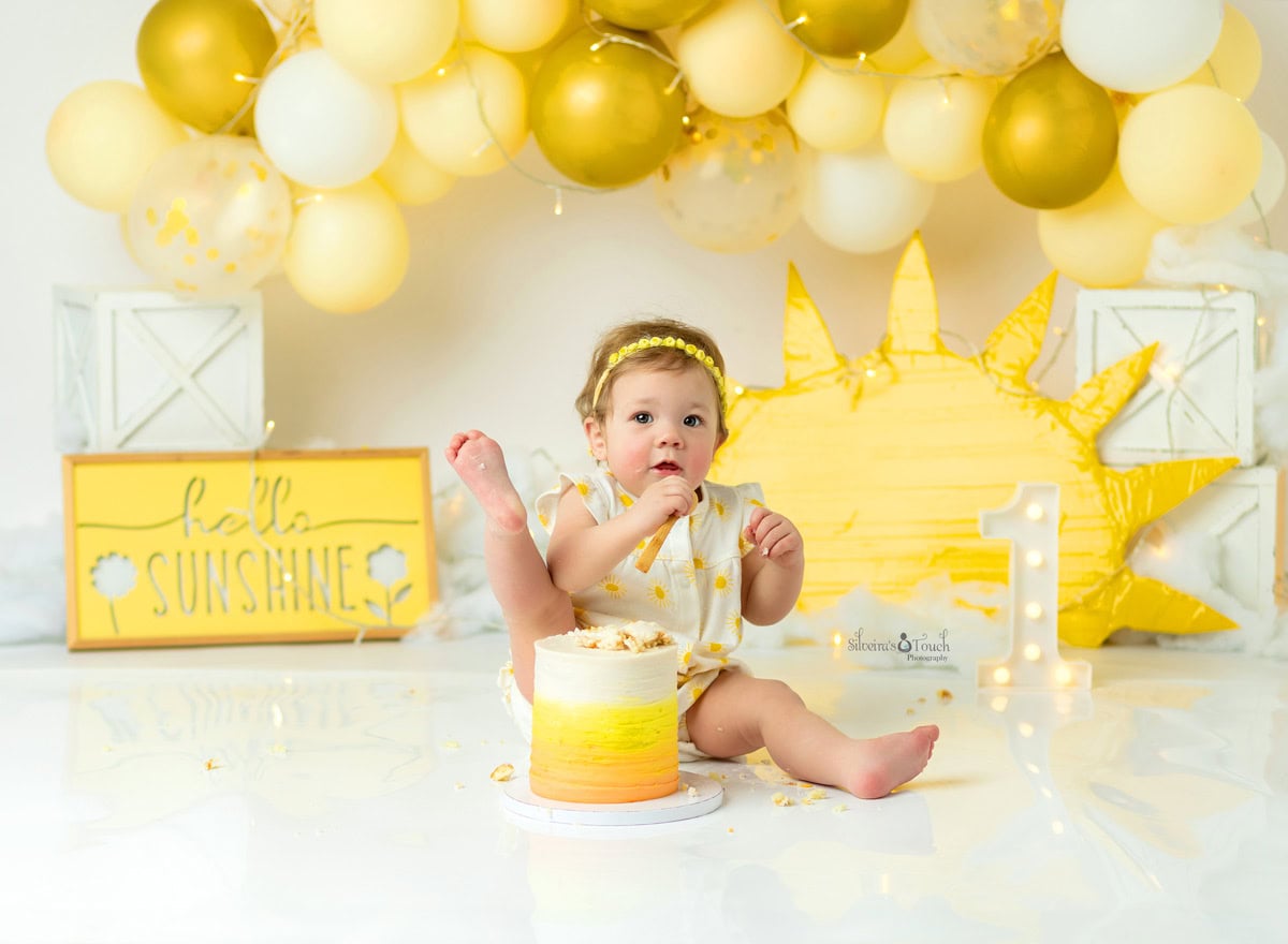 cake smash photos of baby putting her foot on cake and eating a piece with hand