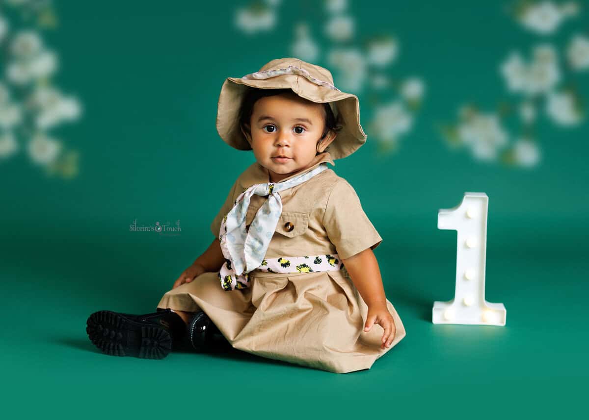Wild One milestone photography of baby wearing a safari outfit on green background