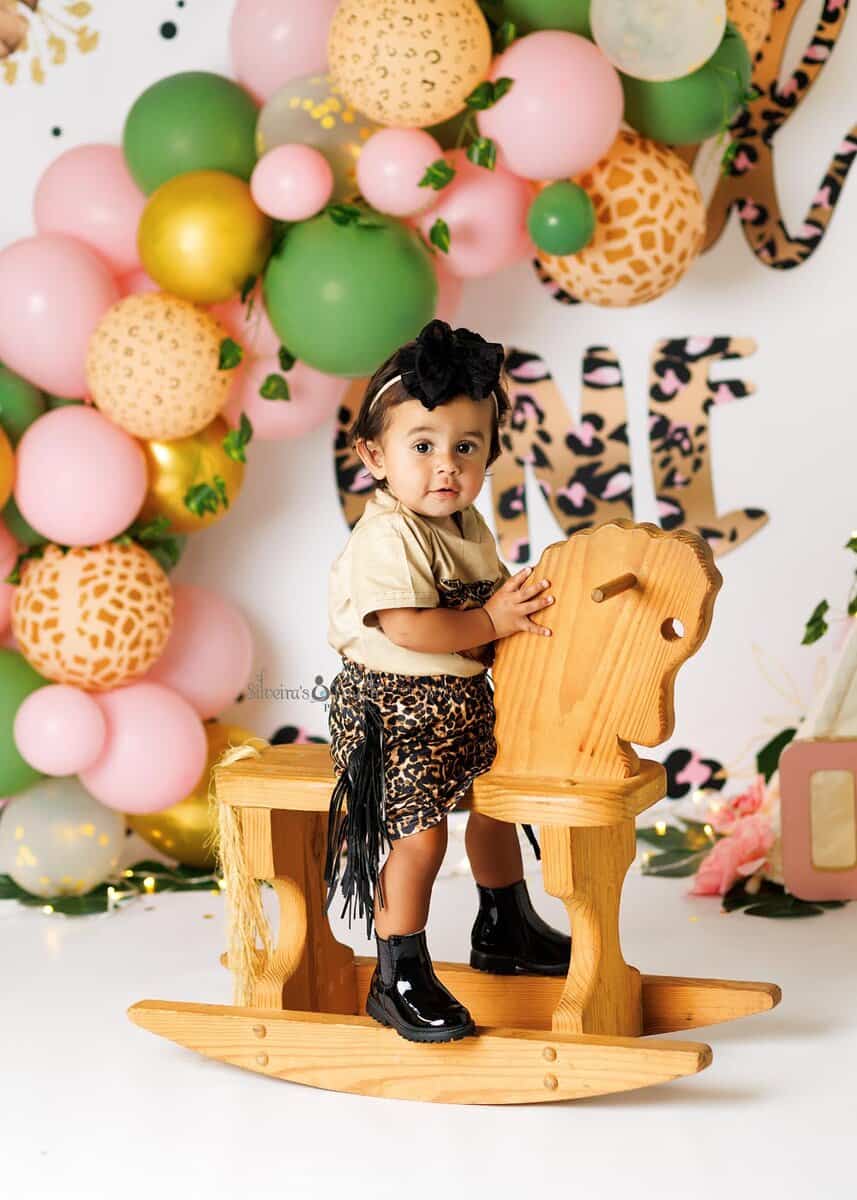 Baby girl in a leopard dress smiling on rocking horse during her first birthday photo session in Dover NJ