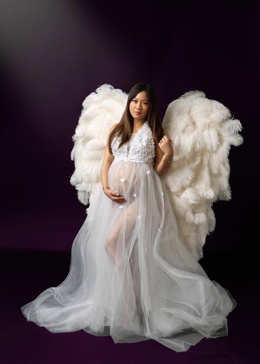 Luxury maternity wardrobe selection featuring elegant gown and feather wings accessories for photoshoot