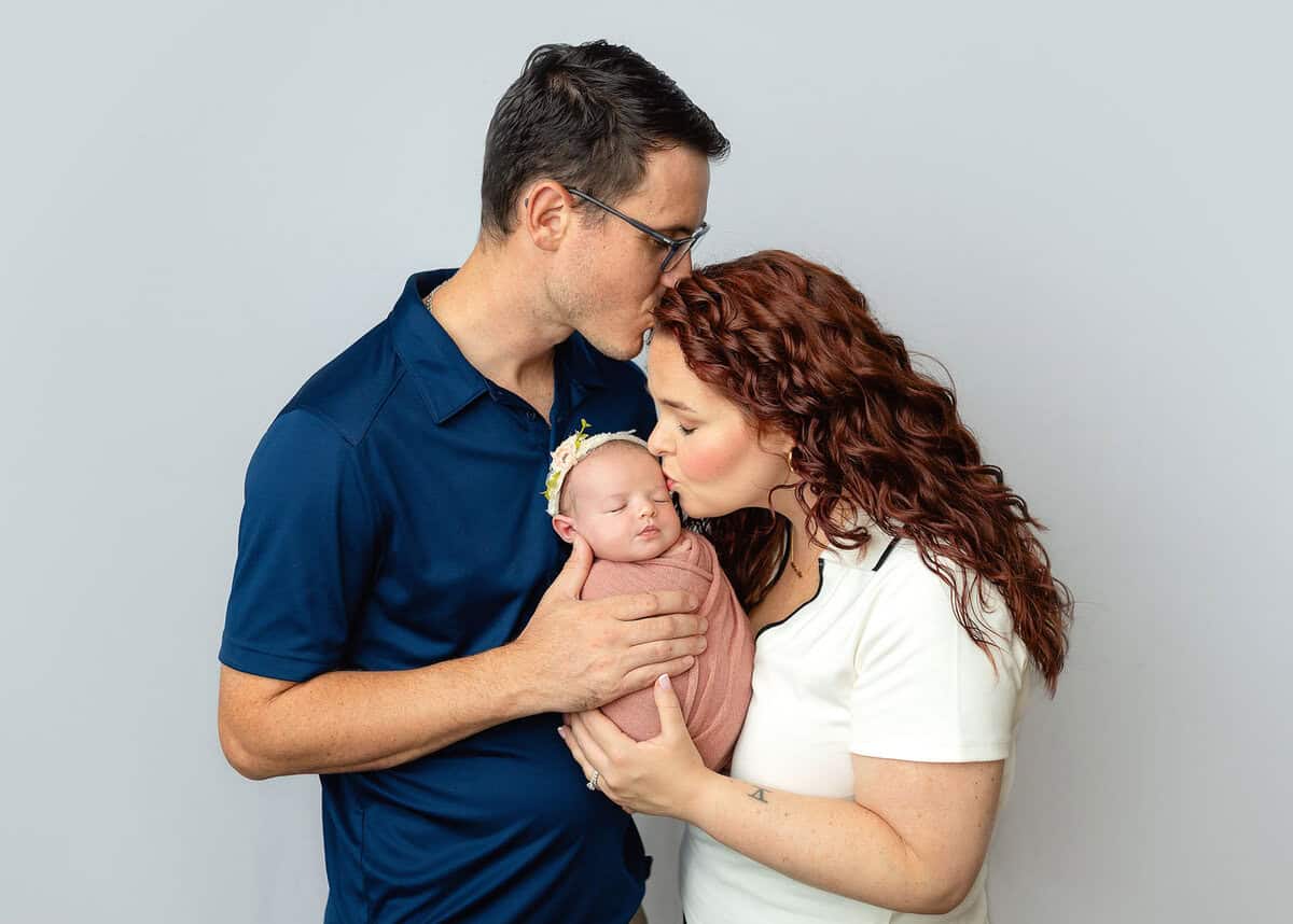 new parents kissing their baby girl wrapped in pink captured in Mount olive NJ by Silveira's Touch Photography